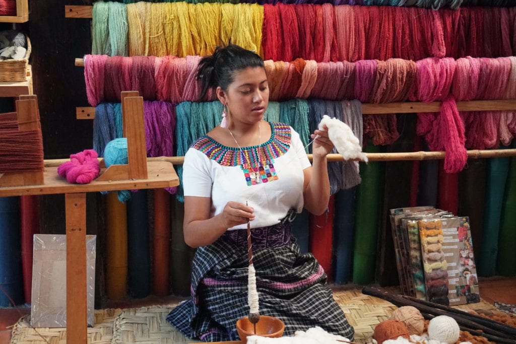 Lady in Mayan dress demonstrating cotton to yarn making